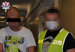 Policjant w żółtej kamizelce trzymający osobę zatrzymaną