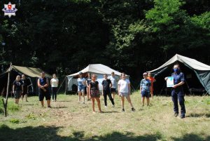 Policjantka na leśnej polanie z dziećmi, w tle namioty.