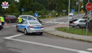 Dwa rozbite samochody stojące na jezdni, policyjne oznakowane radiowozy i policjanci.