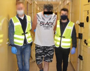 Zatrzymany mężczyzna prowadzony przez policjantów w budynku komendy.