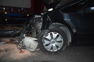 Rozbity przód samochodu znajdującego się na jezdni, w tle samochód ciężarowy.