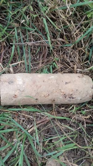 Skorodowany niewybuch leżący na ziemi w trawie.