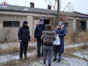 Policjanci i pracownik  ośrodka pomocy ze stojącą tyłem kobietą na tle opuszczonego budynku