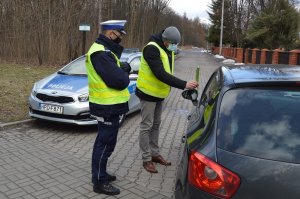 Policjant i mężczyzna w odblaskowej kamizelce z tulipanem w dłoni przy samochodzie w tle radiowóz