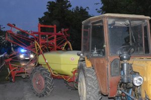 Ciągnik rolniczy z opryskiwaczem, za nim radiowóz