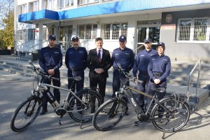 Na tle budynku komendy stoi Komendant Miejski Policji w Chełmie młodszy inspektor Mariusz Kołtun. Na lewo od komendanta członek zarządu województwa lubelskiego pan Zdzisław Szwed, za nim I Zastępca Komendanta Miejskiego Policji mł. insp. Marian Pisklak i policjant. Na prawo od komendanta naczelnik Wydziału Patrolowo-Interwencyjnego komisarz Dariusz Norejko i policjantka. Przed tymi osobami stoją dwa rowery.