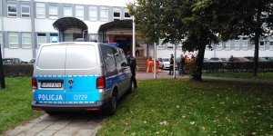 Radiowóz stojący przed budynkiem, w tle osoby biorące udział w ćwiczeniach