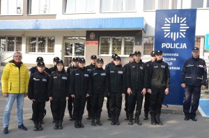 Uczniowie z opiekunem i policjant, w tle budynek komendy.