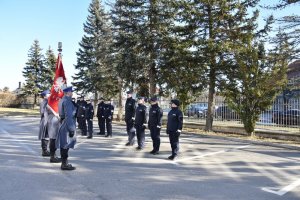 Policjanci stojący na placu, przed nimi poczet sztandarowy komendy.