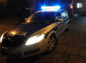 Radiowóz na sygnałach w porze nocnej, w tle budynek.