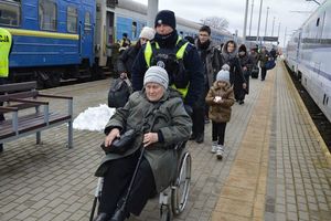 Policjant na dworcu kolejowym pchający wózek inwalidzki z siedzącą na nim kobietą.