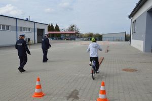 Chłopiec na rowerze jedzie po torze przeszkód po placu obok są policjanci