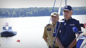 Komendant Wojewódzki Policji w Lublinie udziela wywiadu na spotkaniu z dziennikarzami. W tle zdjęcia Zalew Zemborzycki oraz Policjanci na Łodzi.