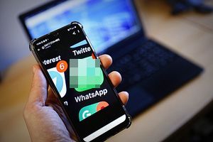 Telefon komórkowy trzymany w dłoni, w tle laptop.