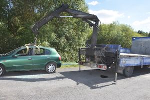 Załadunek samochodu osobowego na ciężarowy za pomocą podnośnika.