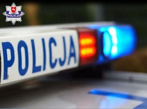 Belka na dachu radiowozu z napisem Policja i włączonymi światłami błyskowymi.