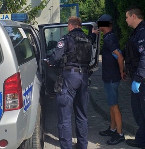 Policjanci z zatrzymanym mężczyzną przy radiowozie.