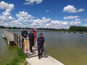 Dwie policjantki, strażak i ratownik wodny na pomoście nad wodą.