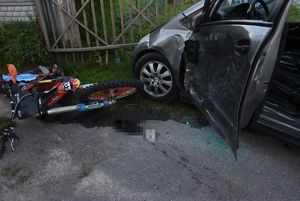 Bok uszkodzonego samochodu i motocykl leżący na drodze.