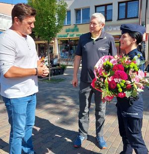 Policjantka z bukietem kwiatów, który otrzymała od dwóch stojących przed nią mężczyzn