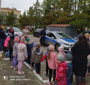 Przedszkolaki na placu oglądają radiowóz, przy którym stoi policjant.