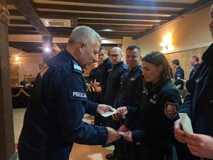 Policjanci łamią się opłatkiem i składają życzenia.