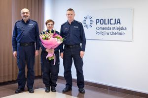 Komendanci z przechodzącą na emeryturę policjantką, która w rękach trzyma bukiet kwiatów.