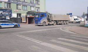 Samochód ciężarowy stojący na jezdni na przejściu dla pieszych. Z lewej strony zdjęcia widoczny jest radiowóz. W tle znajduje się budynek.