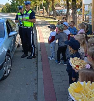 Policjanci prowadza kontrolę oraz dzieci oczekujące z talerzem jabłek i cytryn.