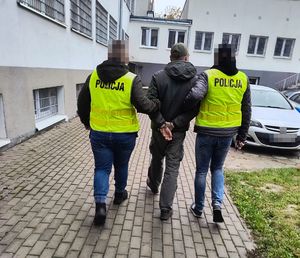 Policjanci prowadzą zatrzymanego mężczyznę.