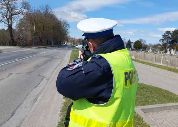 Policjant z miernikiem prędkości przy drodze.
