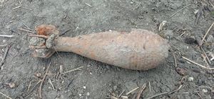 Skorodowany pocisk moździerzowy leżący na ziemi.