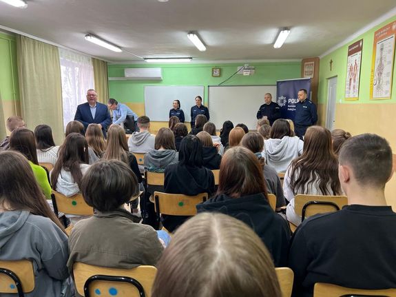 Policjanci, grono pedagogiczne szkoły oraz uczniowie na debacie w sali.