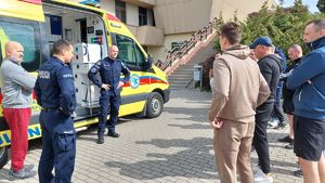 Policjanci i ratownicy medyczni w trakcie instruktażu stoją obok karetki pogotowia.