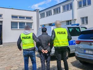 Policjanci prowadzą zatrzymanego mężczyznę.