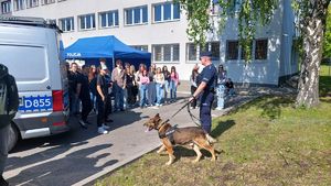 Policjant z psem służbowym przy radiowozie.