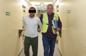 Policjant prowadzi zatrzymanego mężczyznę.