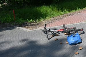 Leżący na kostce brukowej rower, a obok worek z rozsypanymi ziemniakami.