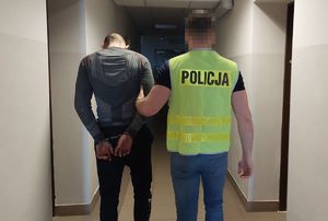 Policjant prowadzi zatrzymanego mężczyznę.