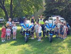 Policjanci ruchu drogowego przy motorach, a obok nich znajdują się dzieci.