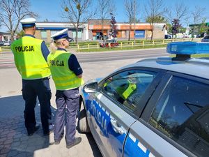 Policjanci przy radiowozie obserwują zachowania uczestników ruchu drogowego.