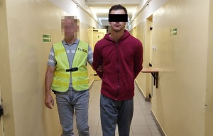 Policjant prowadzi zatrzymanego mężczyznę.