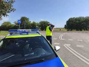 Policjant sprawdza miernikiem prędkość pojazdów, obok radiowóz.