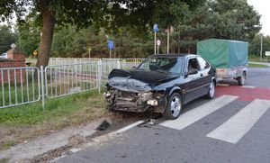 Rozbity samochód z przyczepka stojący na jezdni na przejściu dla pieszych.