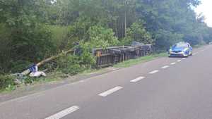 Tir przewrócony na bok w zaroślach, w tle stojący na jezdni radiowóz.