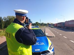Policjant przy radiowozie mierzy prędkość jazdy kierujących.