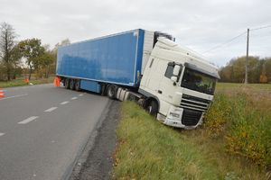 Samochód ciężarowy na jezdni, którego przód stoi w rowie.