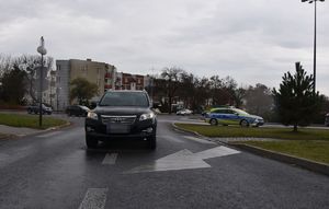 Samochód na jezdni stojący częściowo na przejściu dla pieszych, a w dalszym tle radiowóz