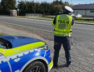 Policjant przy radiowozie prowadzi pomiar prędkości kierujących.