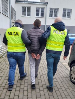 Zdjęcie przedstawiające osobę zatrzymaną prowadzoną przez 2 funkcjonariuszy Policji